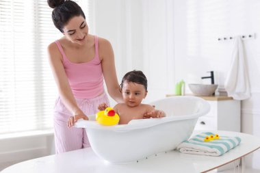 Anne küçük bebeğini evde yıkıyor.