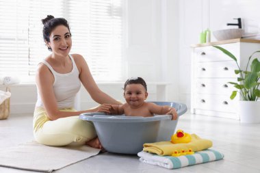 Anne küçük bebeğini evde yıkıyor.