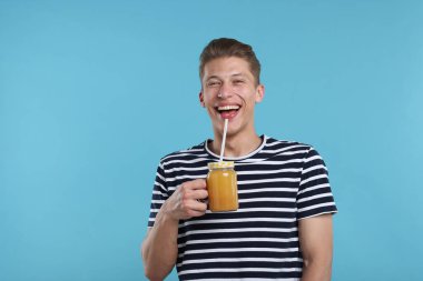Açık mavi arka planda portakal suyu kavanozu olan mutlu bir adam. Tazeleyici içecek.