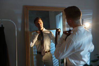 Kapalı alanda aynanın yanında kravat seçen bir adam.