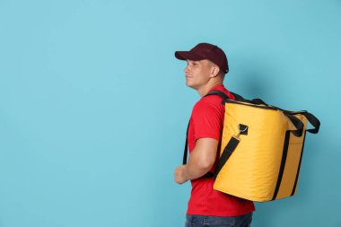 Açık mavi arka planda termo çantalı kurye, mesaj için boşluk. Yemek dağıtım servisi.