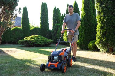 Bahçede çim biçme makinesiyle yeşil çim biçen bir adam