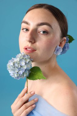 Mavi arka planda hortensiya çiçekleri olan güzel bir kadının portresi.