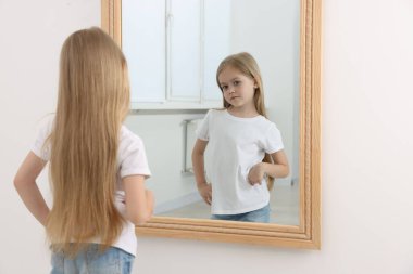 Üzgün küçük kız aynada kendine bakıyor.