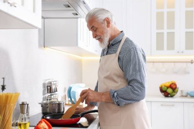 Mutfaktaki mutfağın tepesinde yaşlı bir adam yemek pişiriyor.