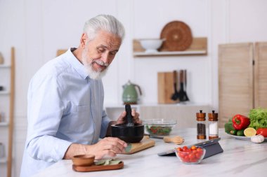 Mutfaktaki beyaz mermer masada yaşlı bir adam yemek pişiriyor.
