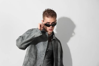 Beyaz arka planda şık ceket ve güneş gözlüğü takan yakışıklı bir genç.