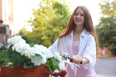 Bisikletin yanında güzel bir genç kız ve şehir caddesinde bir sepet çiçek.