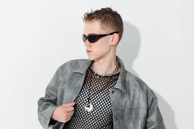 Beyaz arka planda şık ceket ve güneş gözlüğü takan yakışıklı bir genç.
