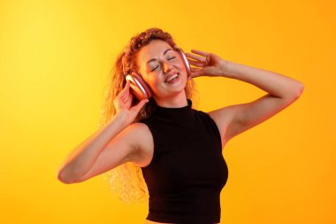 Mutlu kadın kulaklıkla müzik dinliyor ve sarı arka planda dans ediyor.