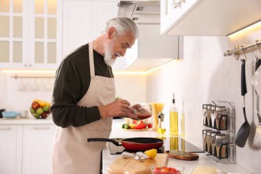 Mutfaktaki mutfağın tepesinde yaşlı bir adam yemek pişiriyor.