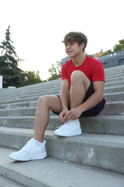 Dışarıda merdivenlerde koşmadan önce bağcıklarını bağlayan genç bir çocuk.