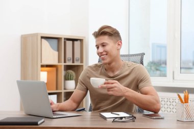 İçerideki ahşap masada dizüstü bilgisayar kullanan bir metin yazarı.
