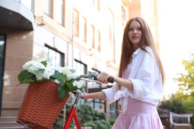Bisikletin yanında güzel bir genç kız ve şehir caddesinde bir sepet çiçek.