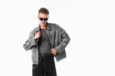 Beyaz arka planda şık ceket ve güneş gözlüğü takan yakışıklı bir genç.