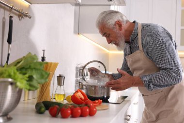 Mutfaktaki mutfağın tepesinde yaşlı bir adam yemek pişiriyor.