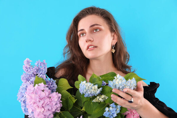 Portrait of beautiful woman with hortensia flowers on light blue background