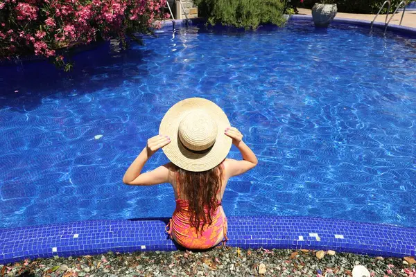 Güneşli bir günde havuz kenarında hasır şapkalı bir kız.