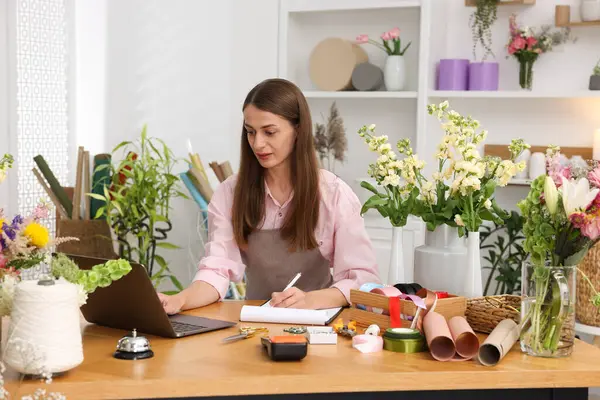 Dükkandaki tahta masada dizüstü bilgisayarla çalışan profesyonel bir çiçekçi.