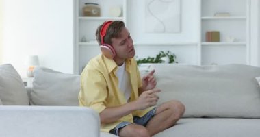 Kulaklıkla müzik dinleyen ve evdeki koltukta dans eden bir adam.