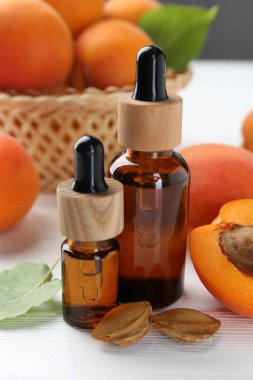 Beyaz ahşap masa üzerinde gerekli yağ şişeleri, taze kayısılar ve çekirdekler, yakın plan.