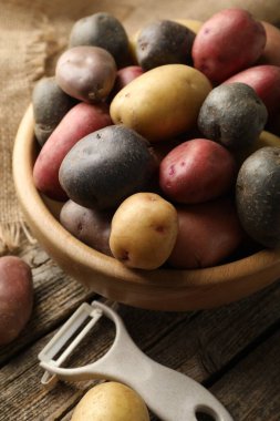 Tabaktaki farklı patatesler ve ahşap masadaki soyucular, yakın plan.