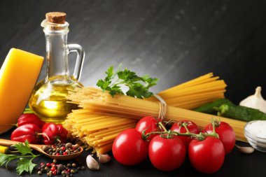 Çiğ spagetti makarnası, ürünler ve baharatlar siyah masa üzerinde koyu dokulu arka plan, yakın plan