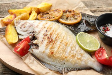 Patates, domates ve ahşap masada limon dilimleriyle servis edilen kızarmış balık. Ev yapımı deniz ürünleri yemeği.
