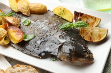Beyaz masada patates, fesleğen ve limon dilimleri ile servis edilen kızarmış balık. Ev yapımı deniz ürünleri yemeği.