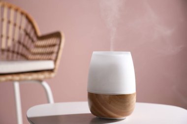 Pembe duvara karşı beyaz masada şık bir aroma lambası, yakın plan.