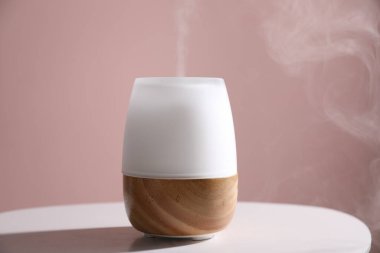 Pembe duvara karşı beyaz masada şık bir aroma lambası, yakın plan.