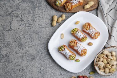 Ricotta peynirli, fıstıklı, şam fıstıklı ve pudra şekerli lezzetli cannoli. Gri desenli masa, düz yatak. Metin için boşluk