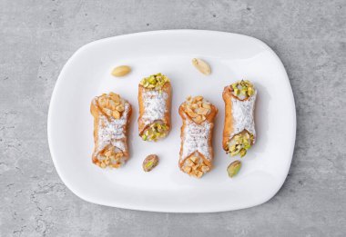 Ricotta peynirli, fıstıklı, şam fıstıklı ve pudra şekerli nefis cannoli. Gri desenli masa, üst manzara.