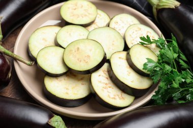 Etrafı maydanozlarla çevrili taze patlıcan dilimleri ve ahşap masa, yakın plan.