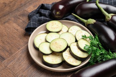 Taze patlıcan dilimleri, bütün olanlar ve maydanozlar ahşap masada, yakın plan.