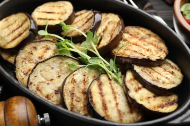 Izgara patlıcan dilimleri ve mikroyeşillikler ahşap masada servis edilir, yakın plan.