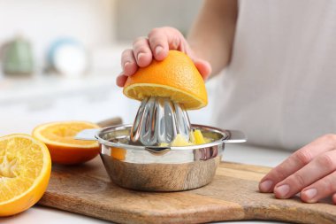 Meyve suyu. İçerideki masada meyve sıkacağı kullanan portakallı kadın, yakın plan.