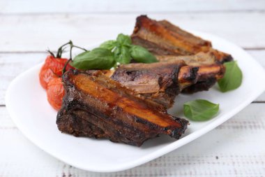 Beyaz ahşap masada kızarmış biftek, domates ve fesleğen, yakın plan.