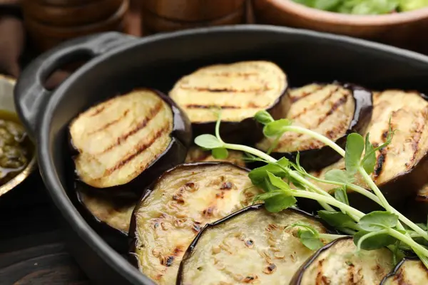 Izgara patlıcan dilimleri ve mikroyeşillikler ahşap masada servis edilir, yakın plan.