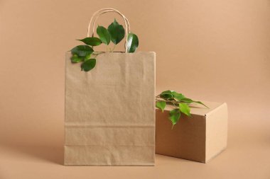 Çevre dostu ambalaj. Kağıt torba, karton kutu ve açık kahverengi arka planda yapraklar.