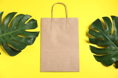 Çevre dostu ambalaj. Sarı arka planda bir kese kağıdı ve yapraklar, düz uzanmış.