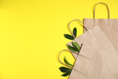 Çevre dostu ambalaj. Sarı arka planda kağıt torbalar ve yapraklar, düz uzanmış. Metin için boşluk