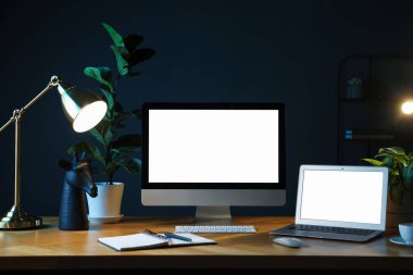 Ofisteki ahşap masa üzerinde modern bilgisayar, dizüstü bilgisayar ve kırtasiye malzemesi olan şık bir iş yeri.