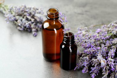 Şişelerdeki yağlar ve gri desenli masadaki lavanta çiçekleri, yakın plan.