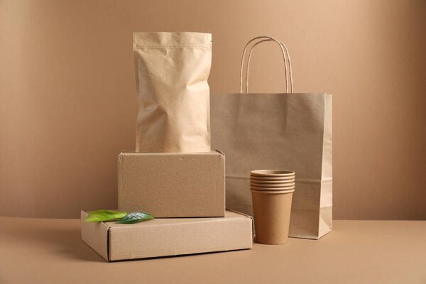 Different eco friendly packaging, cups and leaves on light brown background