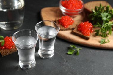 Soğuk Rus votkası ve kırmızı havyarlı sandviçler siyah masada, yakın plan.