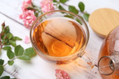 Cam fincanda lezzetli bir gül çayı, beyaz ahşap masada çiçekler ve yapraklar, yakın plan