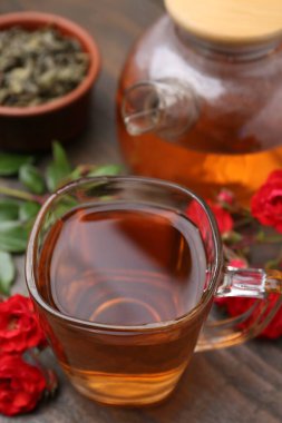 Cam fincanda lezzetli bir gül çayı, tahta masada çiçekler ve yapraklar, yakın plan.