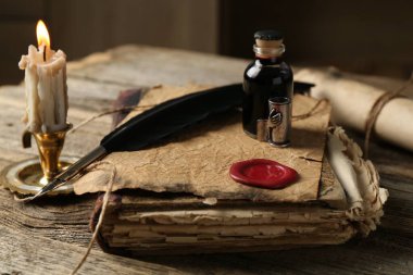 Eski kağıt parşömen, kitap, tüy, mürekkep hokkası ve yanan mum ahşap masa, yakın plan.