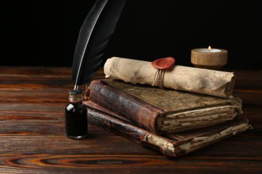 Eski parşömen, yanan mum, tüy, mürekkep hokkası ve ahşap masa üzerindeki kitaplar.